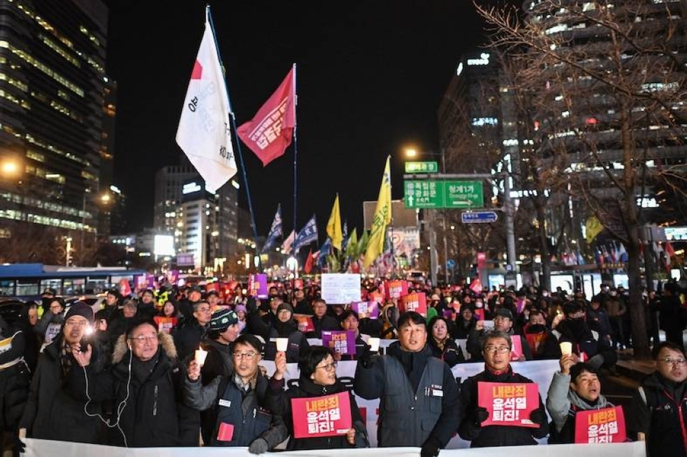 Manifestantes participan en una marcha contra el presidente de Corea del Sur, Yoon Suk Yeol, mientras se dirigen a la Asamblea Nacional en Seúl el 4 de diciembre de 2024. Miles de manifestantes marcharon por el centro de Seúl, cantando y agitando carteles exigiendo la dimisión del presidente después de imponer brevemente la ley marcial y sumir a Corea del Sur en el caos político./AFP,image_description: