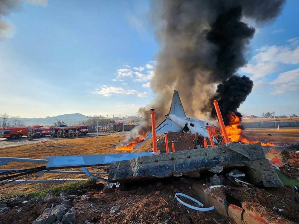 El fuego y el humo se elevan desde la sección de cola de un avión de la serie Jeju Air Boeing 737-800 después de que el avión se estrellara y estallara en llamas en el Aeropuerto Internacional de Muan en la provincia de Jeolla del Sur. / AFP.