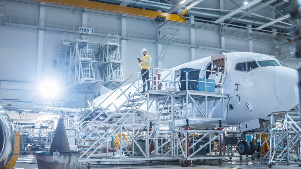 u200bu200bu200bu200bu200bu200bu200bGA Telesis ofrece soluciones y distribución de piezas de aviación comercial. /Fotografía de referencia,image_description:Engineer in Safety Vest Standing next to Airplane in Hangar