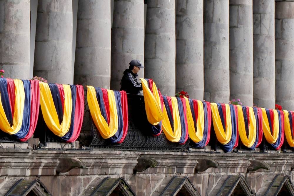 Un hombre cuelga banderas ecuatorianas en el balcón del palacio de gobierno en Quito el 5 de enero de 2025. /AFP,image_description: