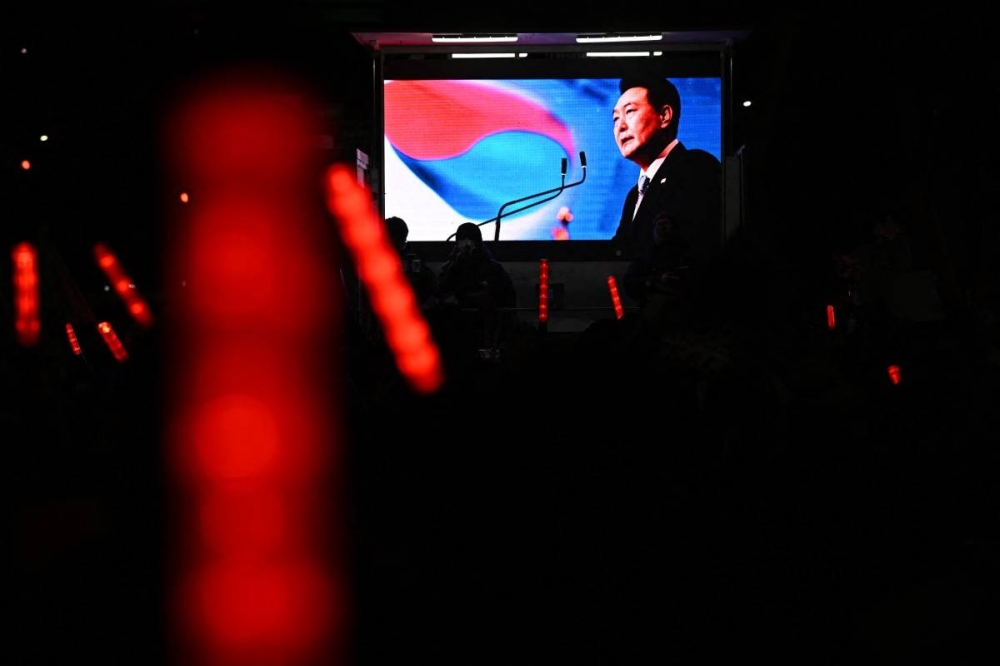 Una pantalla gigante muestra una imagen del presidente de Corea del Sur destituido, Yoon Suk Yeol, mientras sus partidarios sostienen palos de luz durante una manifestación cerca de su residencia en Seúl el 7 de enero de 2025./AFP,image_description: