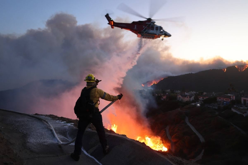 El personal de bomberos responde a las casas destruidas mientras un helicóptero arroja agua mientras el incendio Palisades crece en Pacific Palisades, California/Foto David Swanson AFP.,image_description: