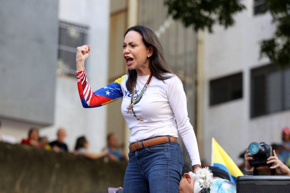 Vestida de blanco, con una bandera y sobre un camión, Machado llegó a la concentración en el barrio comercial de Chacao, en Caracas. /AFP,image_description: