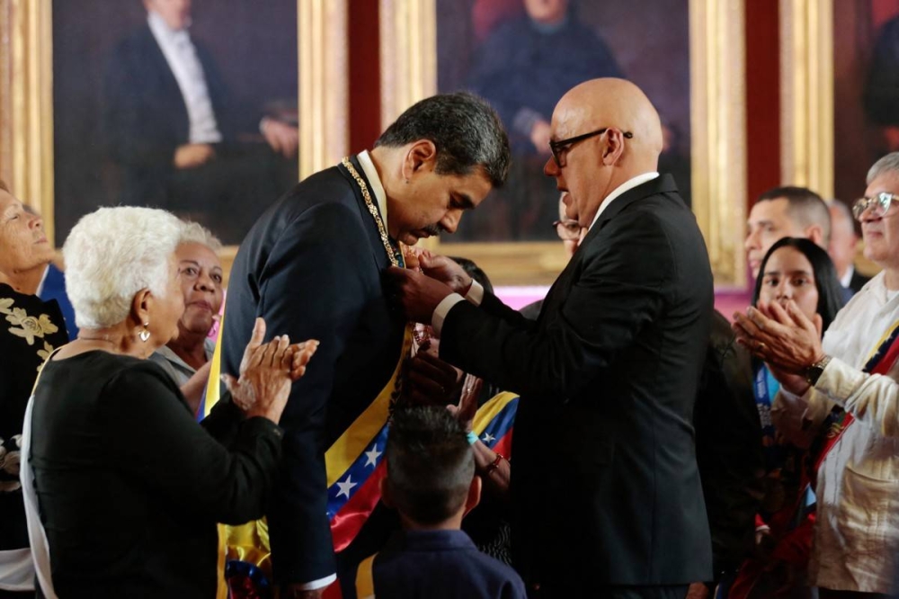 Esta fotografía difundida por la oficina de prensa de la Presidencia de Venezuela muestra al presidente venezolano Nicolás Maduro centroizquierda recibiendo la banda presidencial del presidente de la Asamblea Nacional Jorge Rodríguez durante la investidura presidencial en el Capitolio sede de la Asamblea Nacional en Caracas el 10 de enero de 2025. /AFP,image_description: