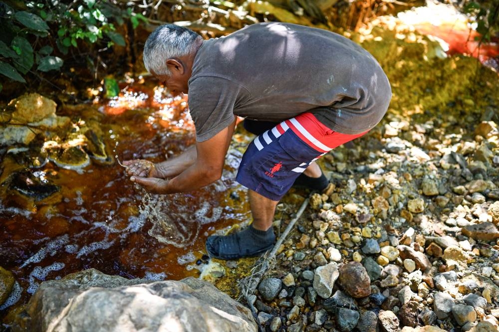 Un hombre se lava las manos en un río contaminado por la actividad minera en Santa Rosa de Lima, departamento de La Unión, El Salvador, el 5 de diciembre de 2024. / AFP.