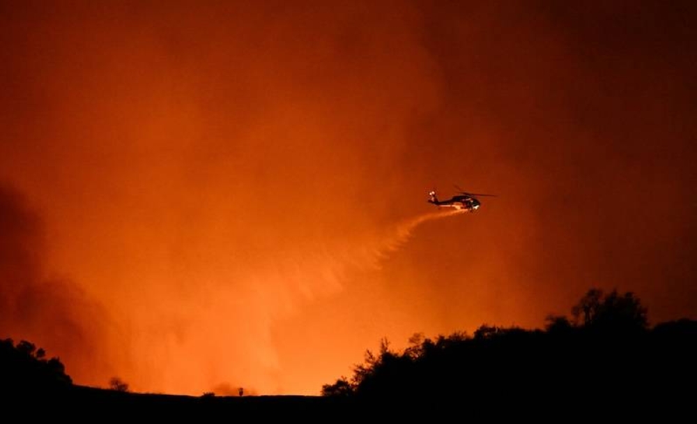 Un helicóptero arroja agua sobre el humo y las llamas del incendio Palisades, que arde detrás de Mulholland Drive en dirección al vecindario de Encino en Los Ángeles, California, el 10 de enero de 2025./ AFP