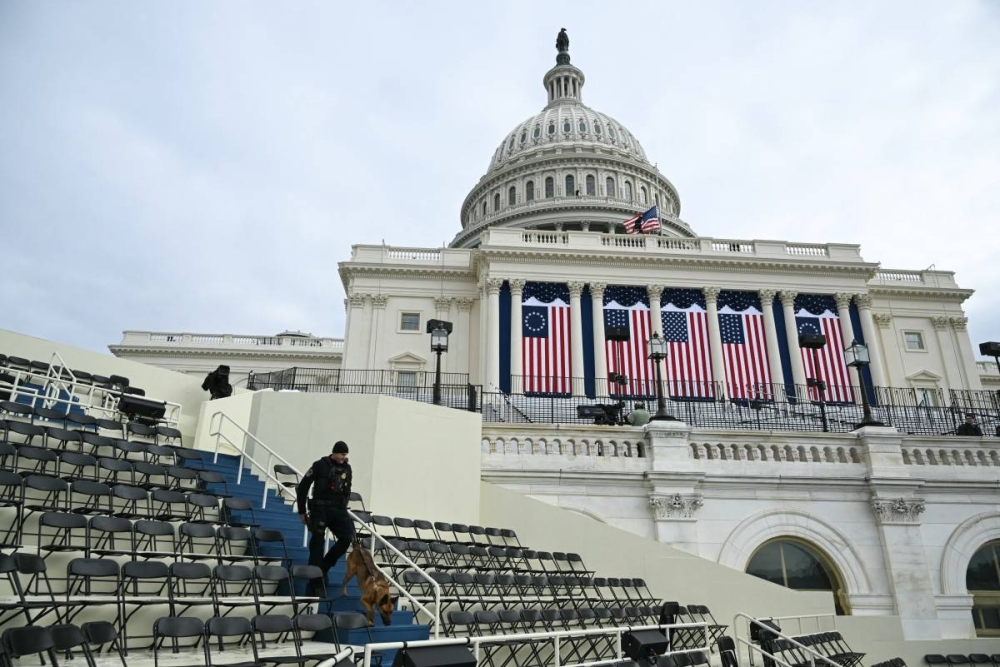 Un oficial de la policía del Capitolio de Estados Unidos camina con un perro K9 en la zona de asientos del escenario de la plataforma en el frente oeste del edificio del Capitolio de Estados Unidos, donde tradicionalmente se lleva a cabo la investidura presidencial, el 17 de enero de 2025, en Washington, DC./AFP,image_description: