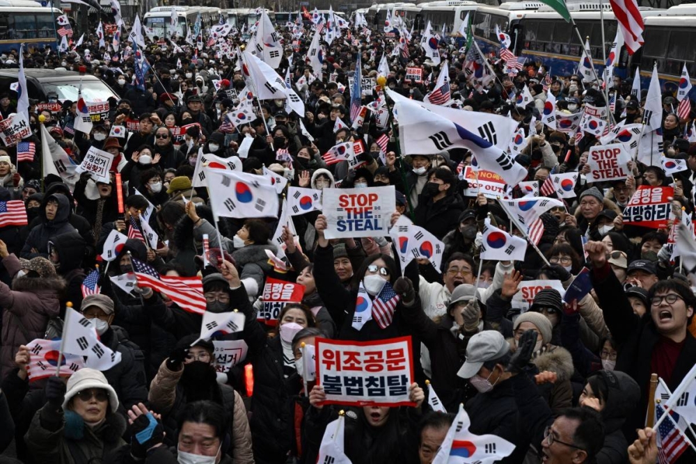 Los partidarios de Yoon ondean banderas mientras se reúnen en una calle frente al Tribunal del Distrito Oeste de Seúl, en Seúl, el 18 de enero de 2025, mientras el tribunal evalúa si extender la detención del presidente de Corea del Sur enjuiciado, Yoon Suk Yeol, después de que los investigadores lo arrestaran por un intento fallido de instaurar la ley marcial. Yoon, quien ha afirmado que su arresto e investigación son ilegales, sumió al país en el caos el 3 de diciembre cuando intentó suspender el gobierno civil, citando la necesidad de combatir las amenazas de 