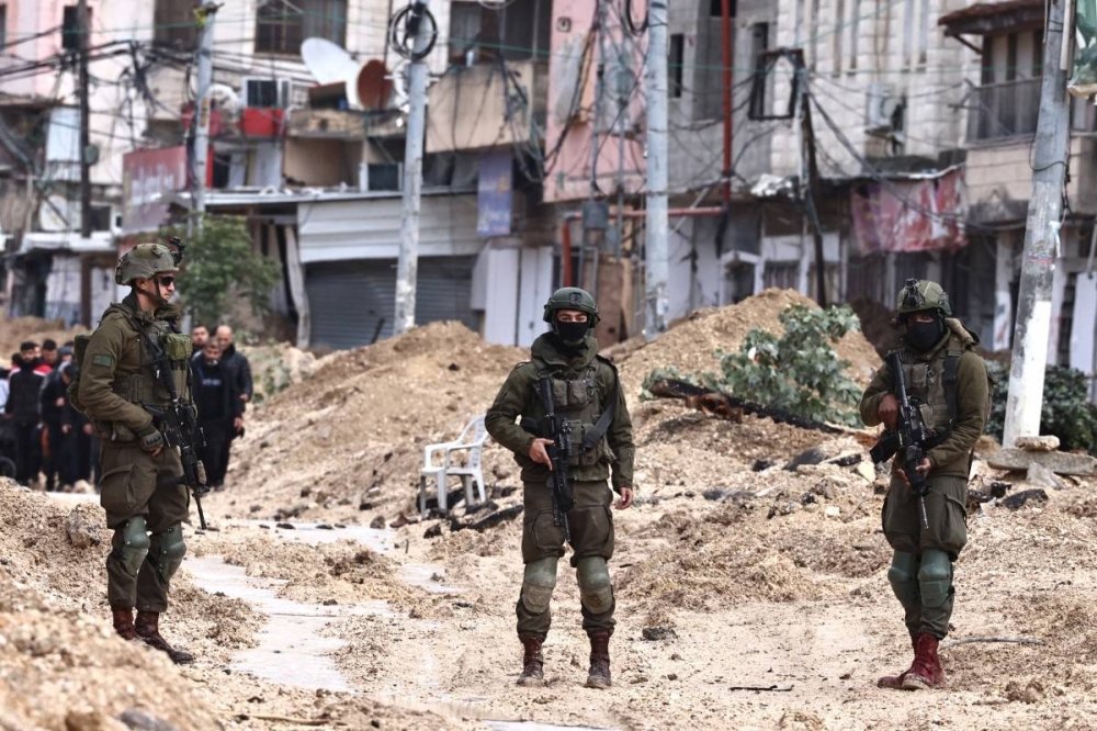 Los soldados israelíes vigilan cómo los palestinos abandonan sus hogares en busca de seguridad durante una redada del ejército en el campo de refugiados de Nur Shams, cerca de Tulkarem, en la Cisjordania ocupada, el 10 de febrero de 2025/Foto Zain Jaafar AFP.,image_description: