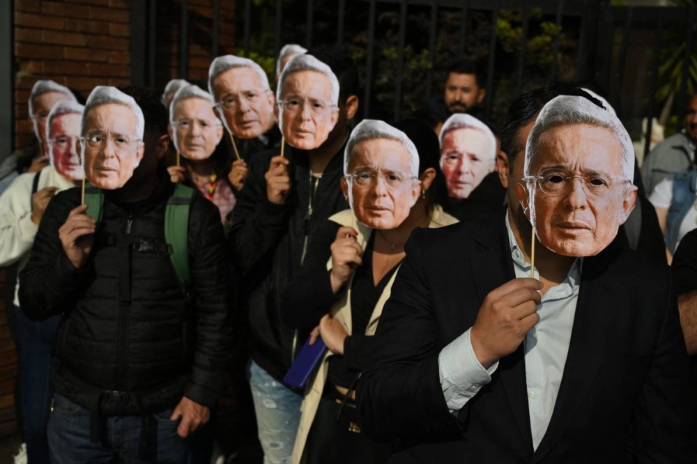 Partidarios del expresidente colombiano Álvaro Uribe portan máscaras con su imagen mientras se manifiestan afuera de su juicio en Bogotá el 10 de febrero de 2025. Photo by Raul ARBOLEDA / AFP,image_description: